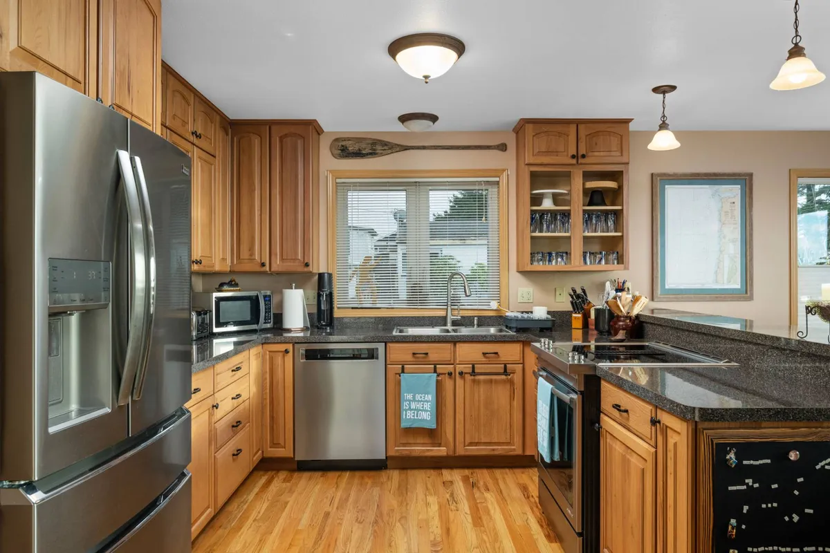 The recently remodeled kitchen is showcased with sleek stainless steel appliances, warm wood cabinetry, and granite countertops. A window above the sink provides even more coastal views, while touches like a decorative paddle add coastal charm. The scene invites both cooking and socializing.