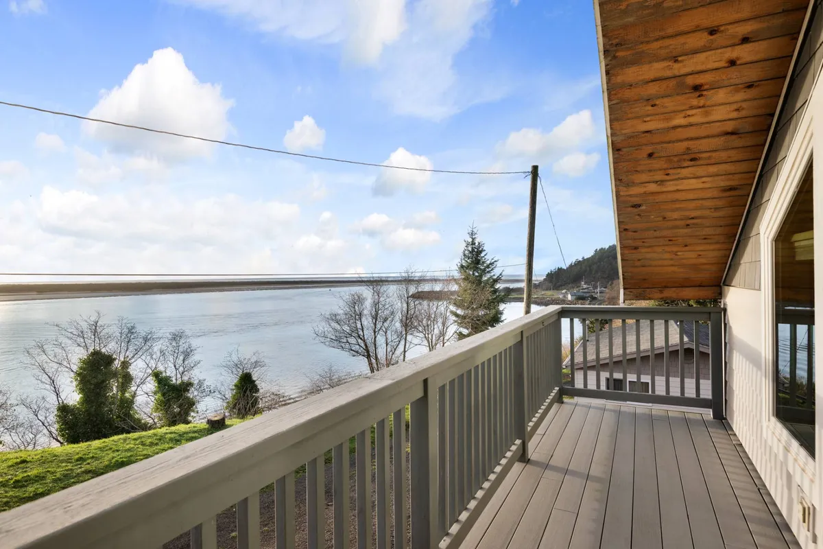 The image showcases a serene exterior view of Pirate's Bluff, featuring a spacious deck with railings overlooking unobstructed bay and ocean vistas. Lush greenery surrounds the property, enhancing the peaceful ambiance. The deck invites guests to relax, sip morning coffee, host outdoor gatherings, or watch the sun rise over the water.