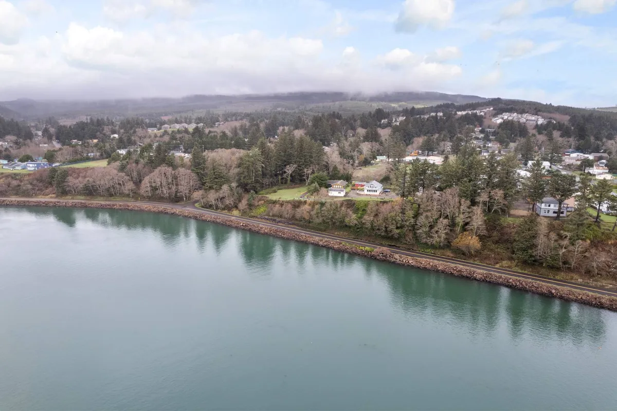 This image captures a calm water surface bordered by a tree-lined shore and houses along the waterfront. The natural setting is serene, inviting exploration, boating, or quiet walks along the shore at sunset.