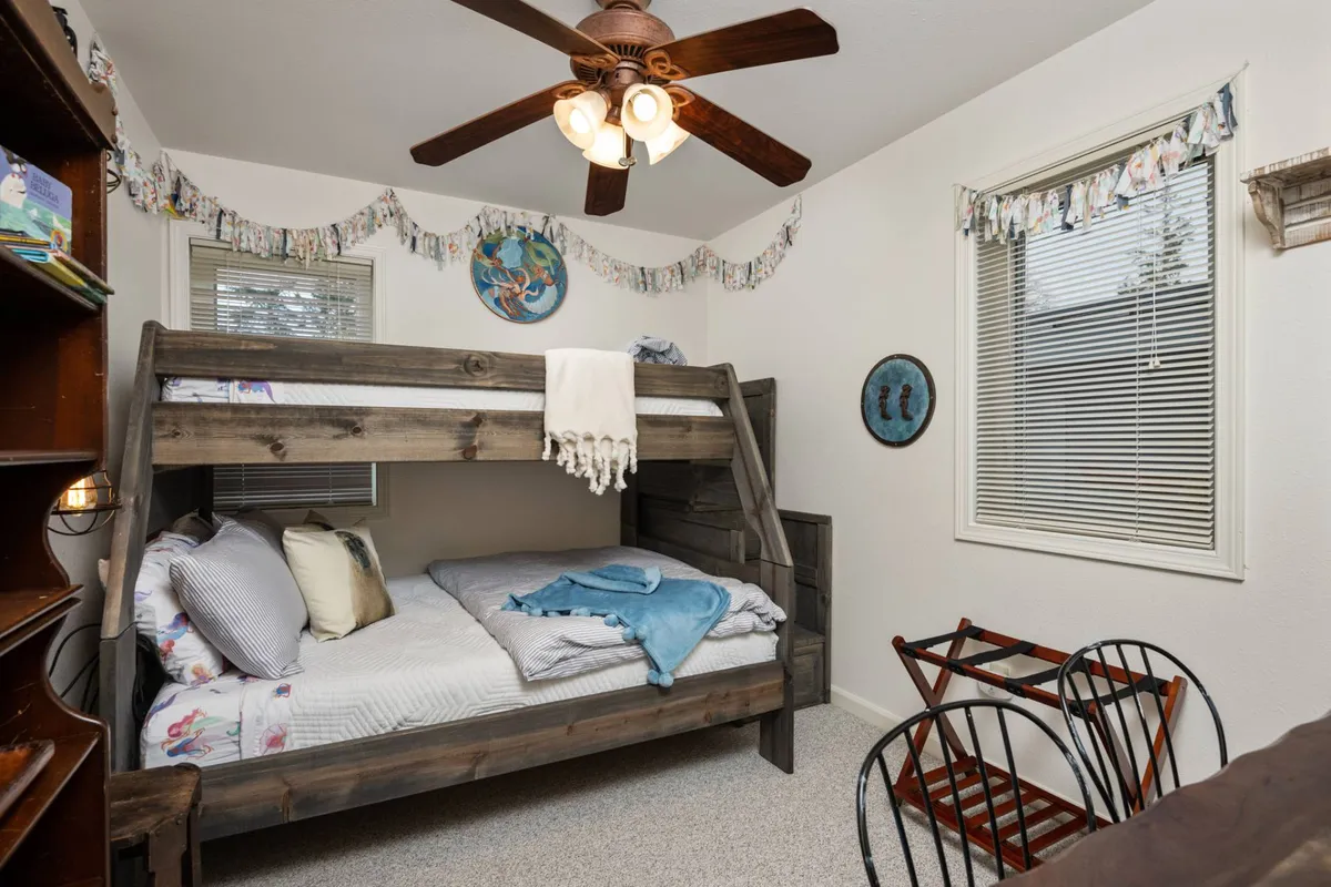 A playful bedroom with a bunk bed, decorative wall hangings, and ceiling fan, designed for sleep, reading, or games. The inviting decor suggests a space suited for siblings, friends, or multigenerational stays.