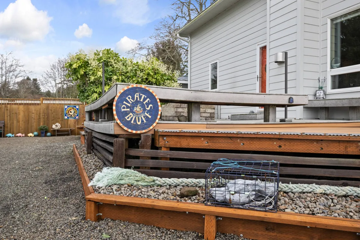 This exterior image highlights the pirate-themed sign, a welcoming wooden deck, decorative rope, and fishing trap, creating a whimsical and inviting entryway. The deck is surrounded by greenery, suggesting a private outdoor oasis ideal for relaxation or sharing a morning coffee.