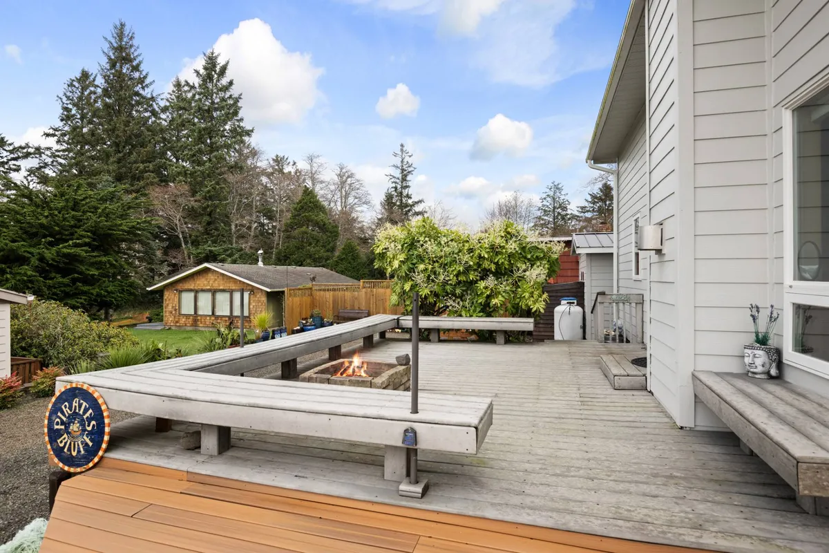 An inviting outdoor seating area with a fire pit is surrounded by lush greenery. The space is designed for group gatherings, with comfortable chairs and a warm, welcoming atmosphere, perfect for sharing stories after a day of beachcombing or tide pool adventures.