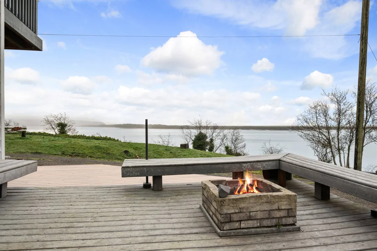 A cozy outdoor fire pit area is shown here, with comfortable seating arranged for group gatherings. Beyond the fire pit, there’s a striking view of the water, setting up the perfect backdrop for storytelling, roasting marshmallows, and stargazing beneath the open sky.