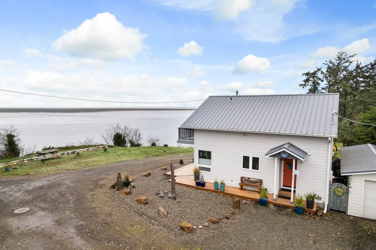 This image captures the exterior of the house with a spacious deck overlooking the water, featuring a seating area ideal for relaxation. The tranquil scene showcases the seamless transition between indoor and outdoor living, with the inviting deck that connects directly to the home and provides panoramic bay and ocean views.
