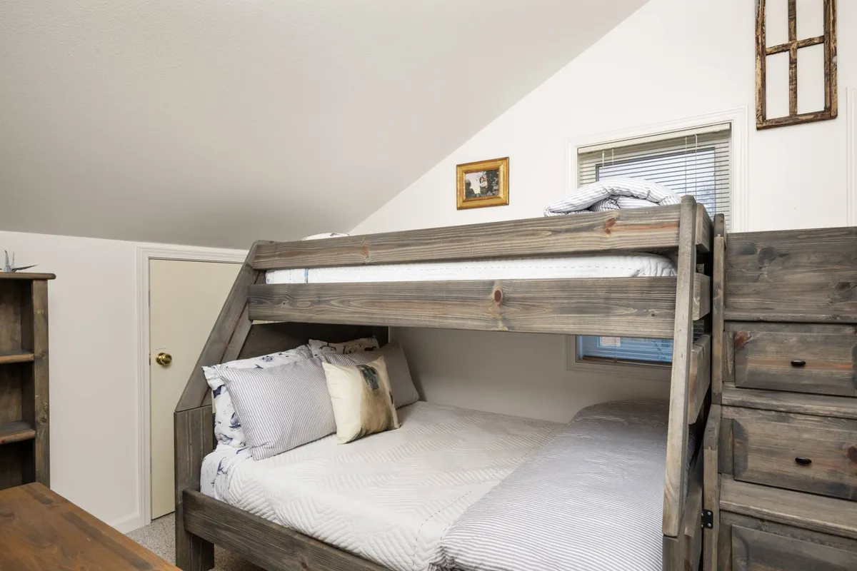A cozy bedroom featuring a twin-over-full bunk bed, a wooden dresser, and framed pictures on the wall. The space is welcoming and clearly designed with children or families in mind, offering a comfortable and playful sleeping arrangement.