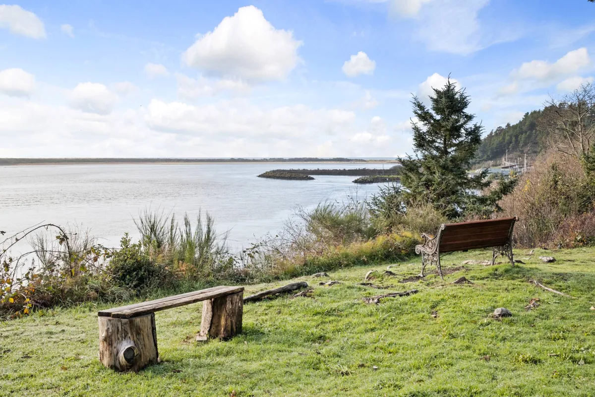 A wooden bench overlooks a serene body of water, with distant trees lining the opposite shore. The setting feels peaceful and offers a spot for relaxation, sunset watching, or birdwatching, making it an ideal place for families to gather and enjoy the natural beauty together.