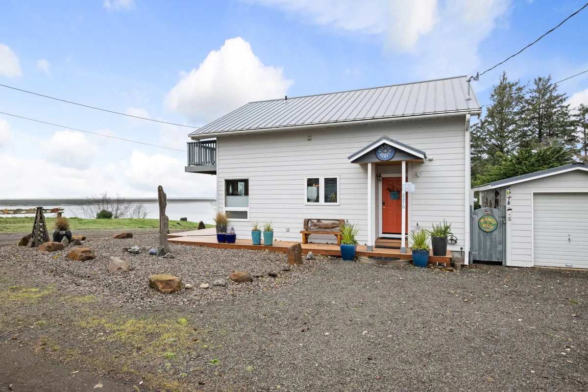 This exterior image highlights the home's entrance, a spacious deck area with garden planters, and appealing rock landscaping. The deck overlooks the water, suggesting a tranquil spot for morning coffee, social gatherings, or simply soaking in the views.