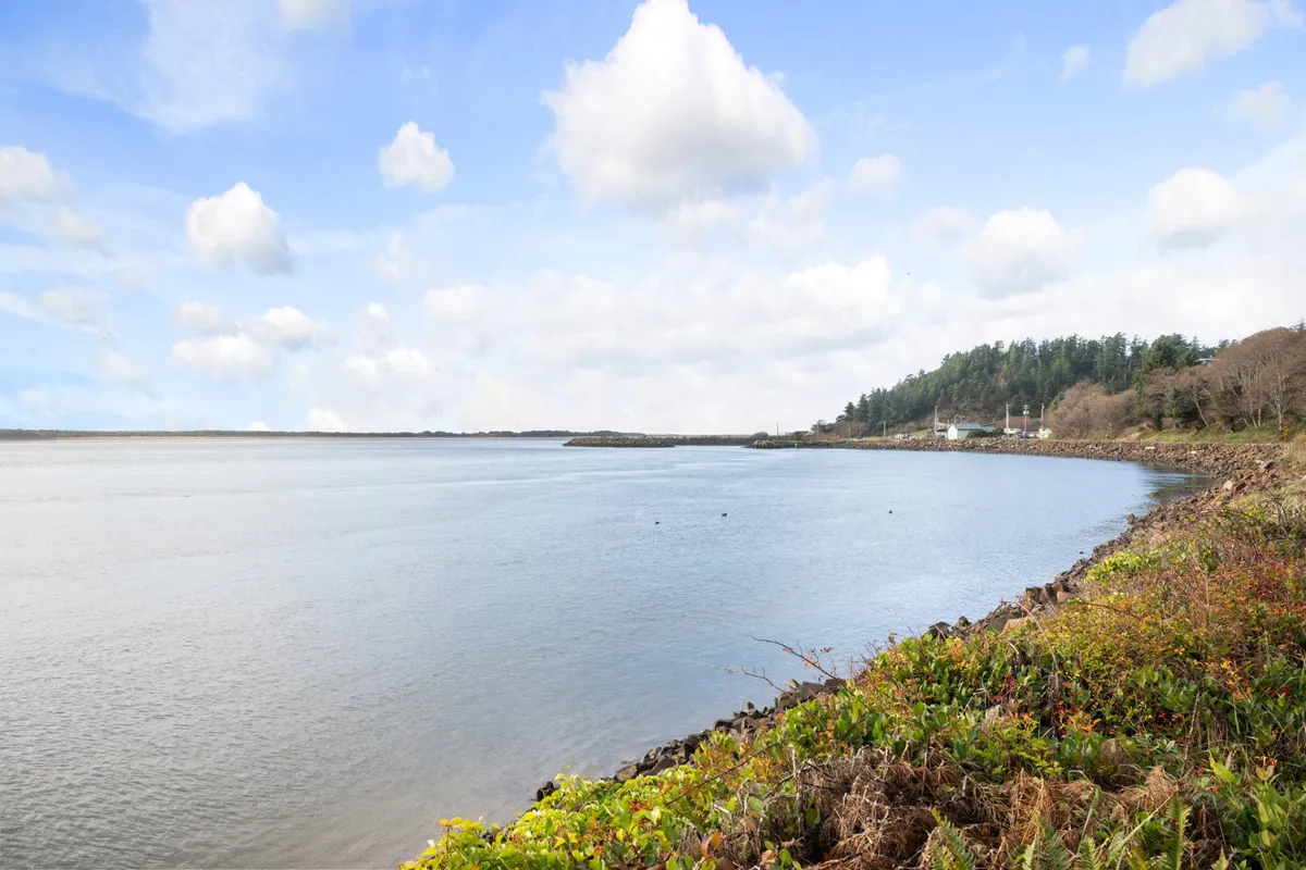 A tranquil view over calm waters lined by lush greenery and a distant shoreline. The scene offers expansive, uninterrupted sightlines, ideal for capturing sunsets, observing birds, or photographing shifts in light and weather.