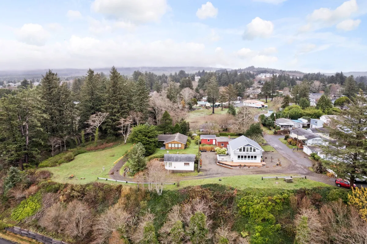 A wide view of the property showing the main house with large windows, several smaller houses, an expansive green lawn, and surrounding trees. The peaceful, spacious setting is ideal for couples to reconnect or find inspiration for remote work.