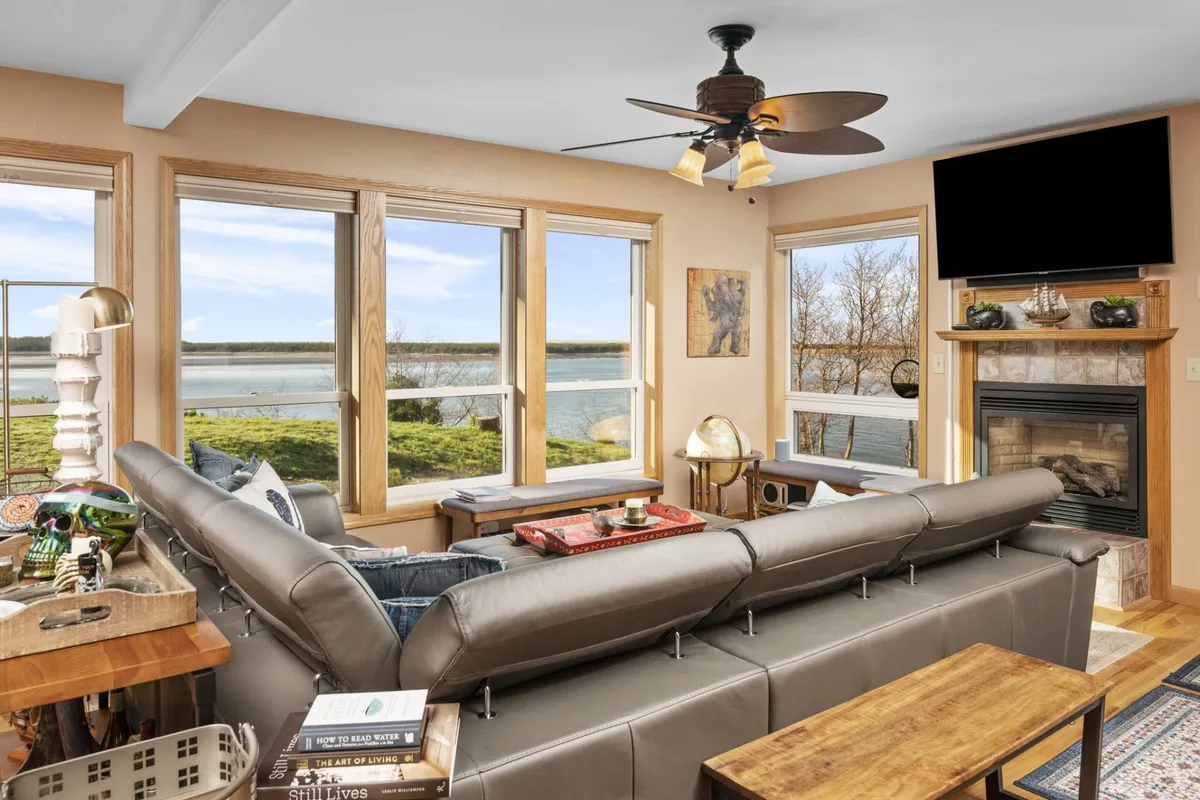 A cozy living room with a plush sofa, fireplace, and expansive windows looking out to the water. The space is designed for relaxation and togetherness, reinforcing the sense of tranquility and seclusion.